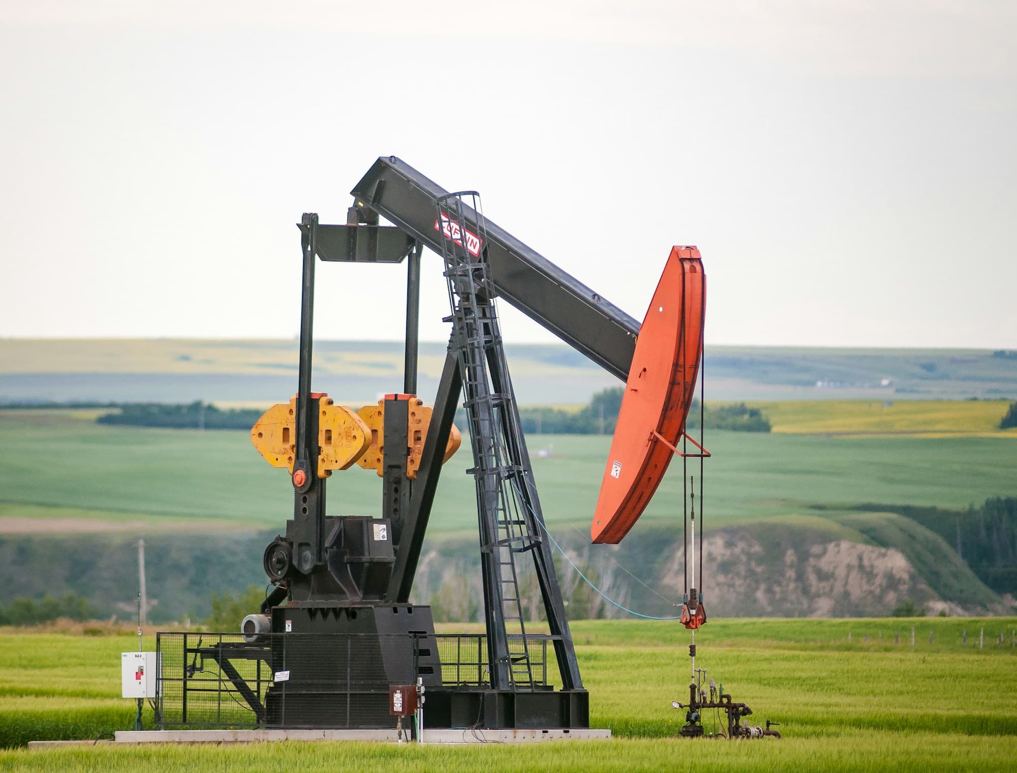 Black and orange pumpjack in a green field with rolling farmland behind