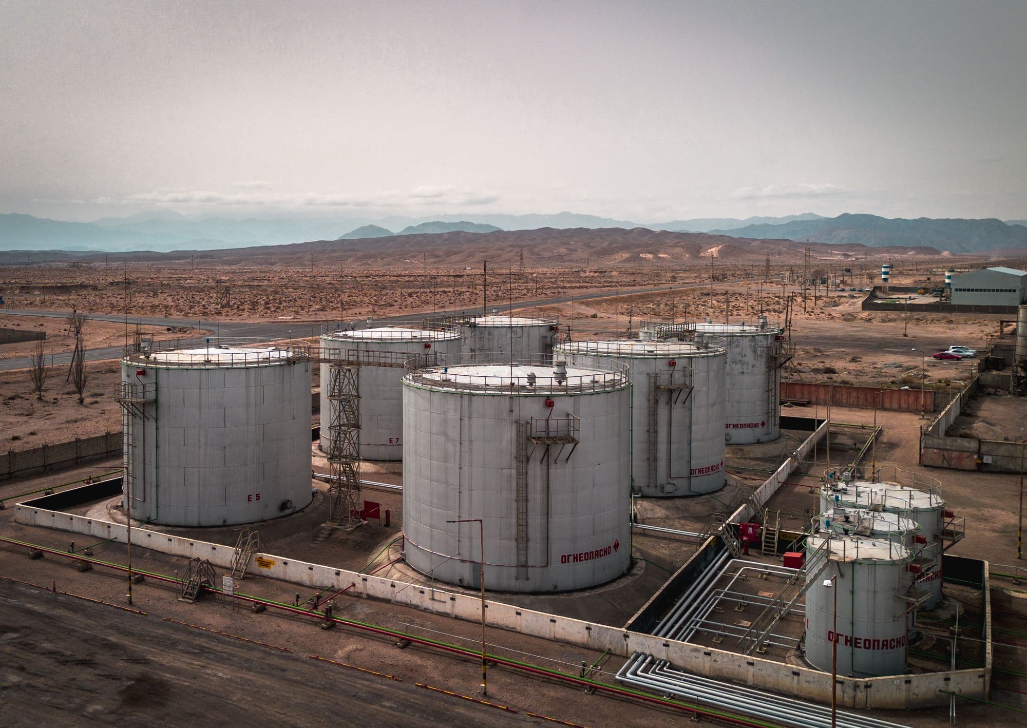 Aerial view of large white storage tanks on a desert plain with mountains beyond