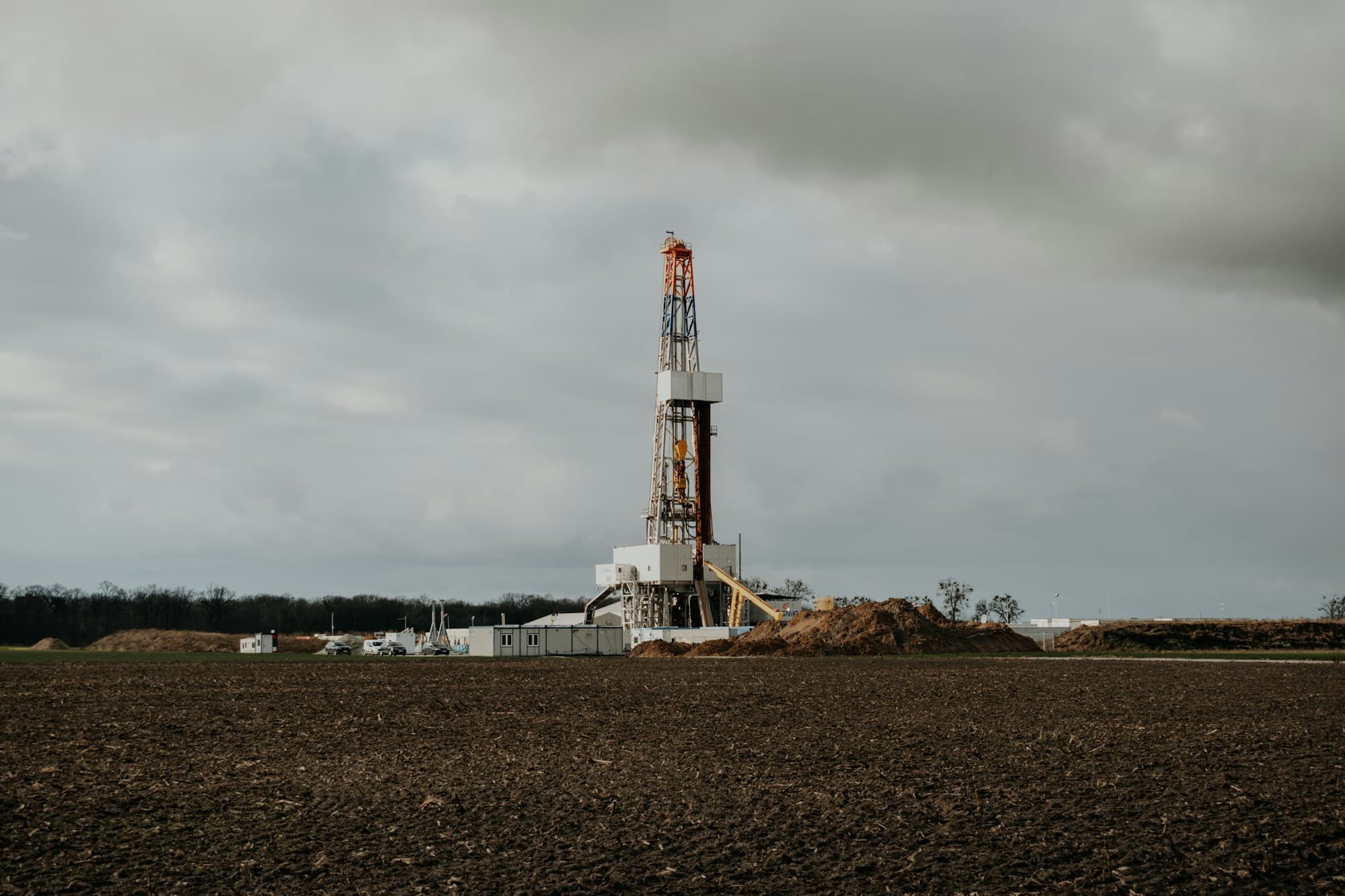 Drilling rig standing in a ploughed field under a dark overcast sky